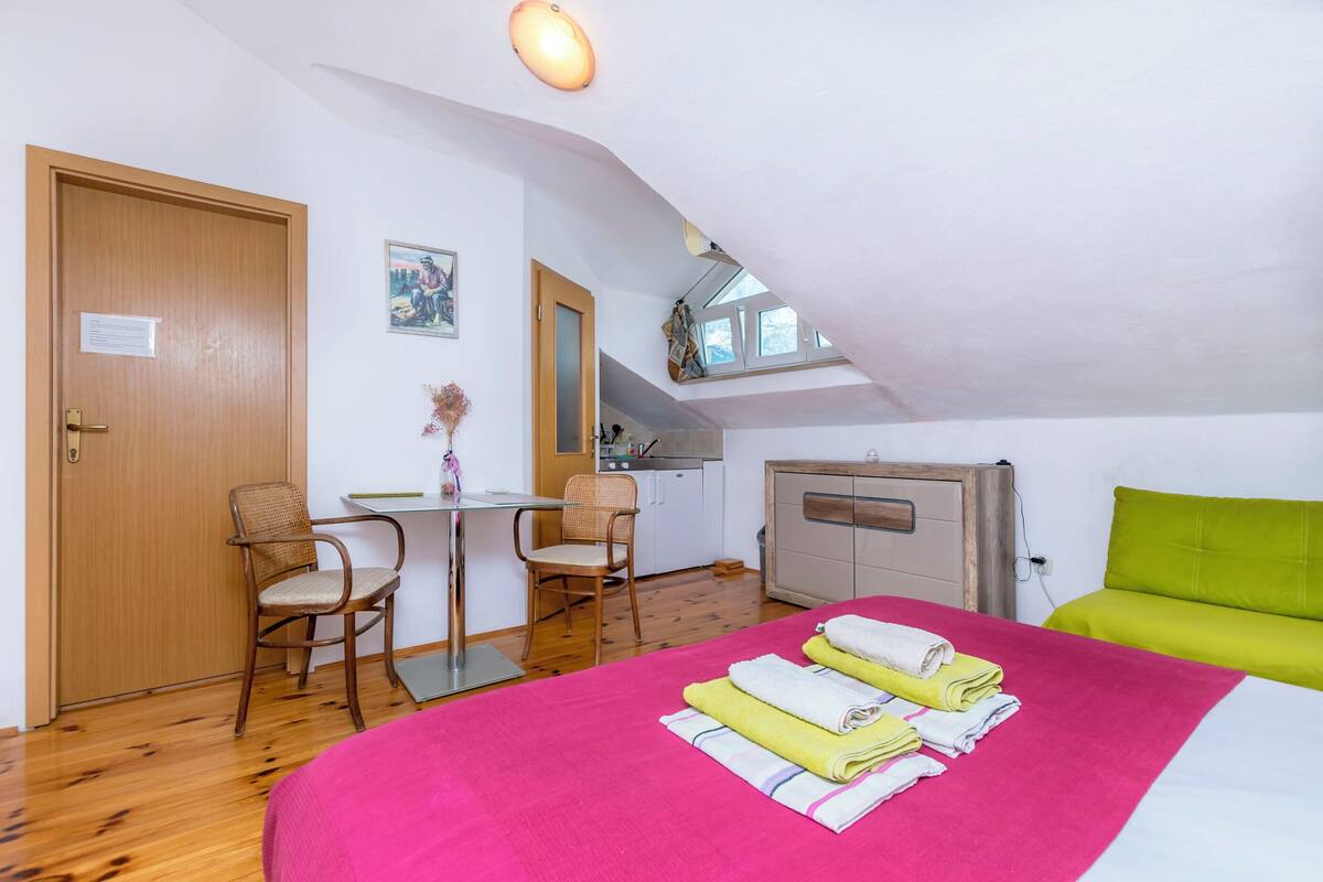 A room with a bed, a desk, two chairs, a kitchenette, and a window.