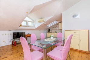 A dining area with a glass table and pink chairs, a kitchen with a microwave, and a TV in the background.