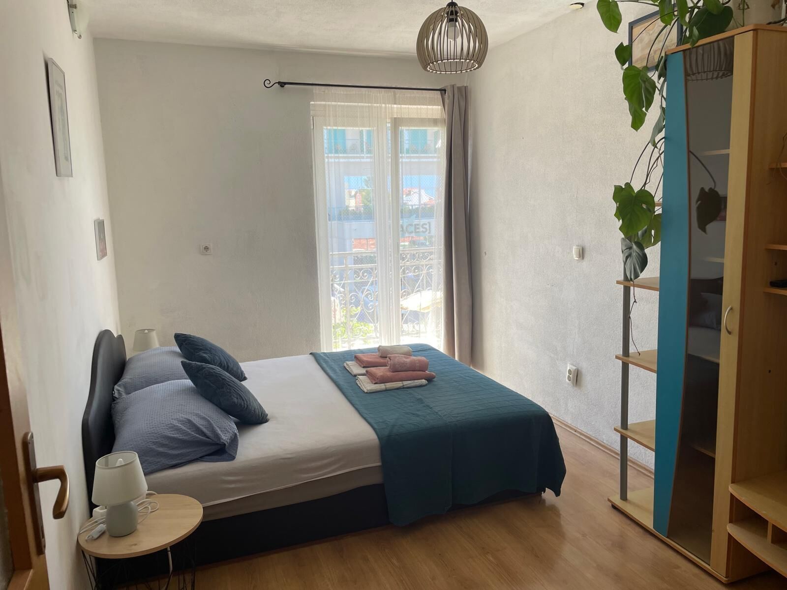 A bedroom with a bed, bedside table, lamp, window with curtains, and a plant.
