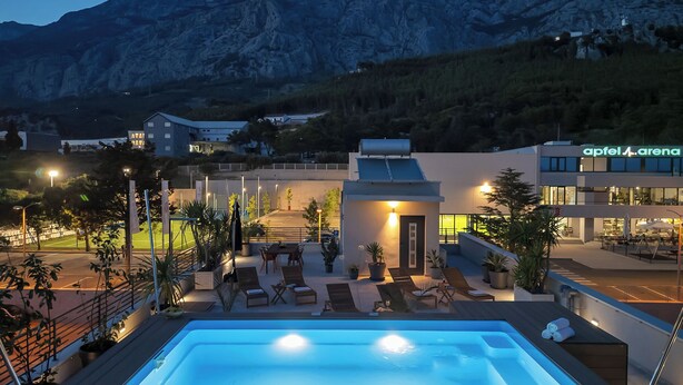 A hotel with a rooftop pool, lounge chairs, and a mountain backdrop. - Apartment Luxury Wellness (Makarska)