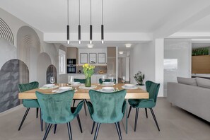A modern dining area with a wooden table, teal chairs, and pendant lighting. - Apartment Luxury Wellness (Makarska)