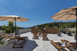 A rooftop terrace with lounge chairs, umbrellas, and potted plants. - Apartment Luxury Wellness (Makarska)