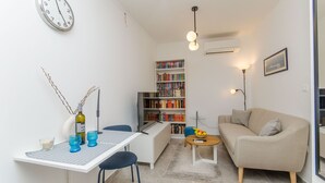 A compact living space with a dining table, a sofa, a bookshelf, and a wall clock. - Apartment Sunny Dream (Kastel Novi)