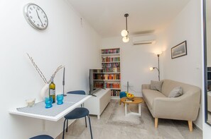A compact living space with a dining table, a sofa, a bookshelf, and a wall clock. - Apartment Sunny Dream (Kastel Novi)