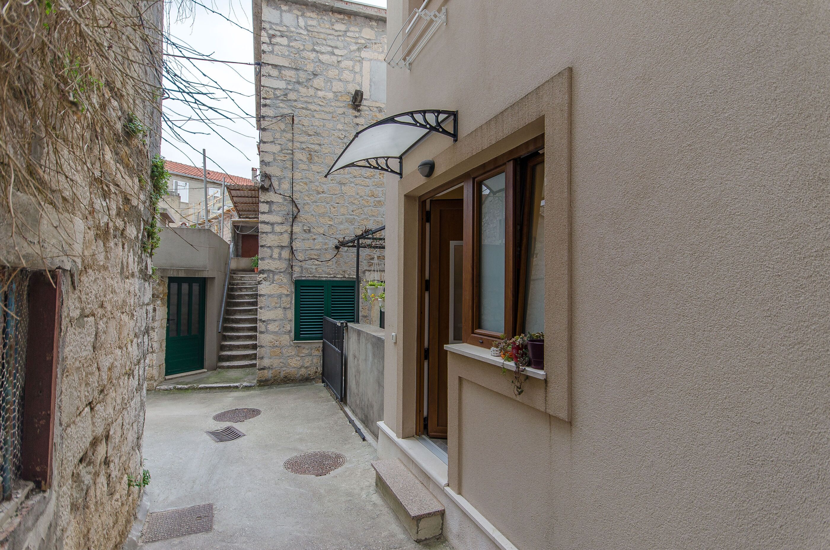 A narrow alleyway with a stone wall, a wooden door, and a window with a plant.
