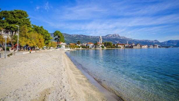 A coastal town with a beach, clear water, and mountains in the background. - Apartment Sunny Dream (Kastel Novi)