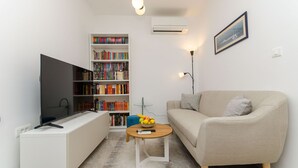 A living room with a flat-screen TV, a bookshelf, a sofa, a coffee table with fruit, and a framed picture on the wall. - Apartment Sunny Dream (Kastel Novi)