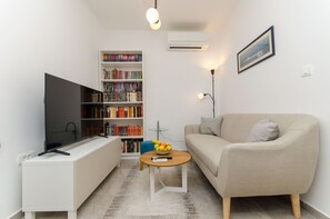 A living room with a flat-screen TV, a bookshelf, a sofa, a coffee table with fruit, and a framed picture on the wall. - Apartment Sunny Dream (Kastel Novi)