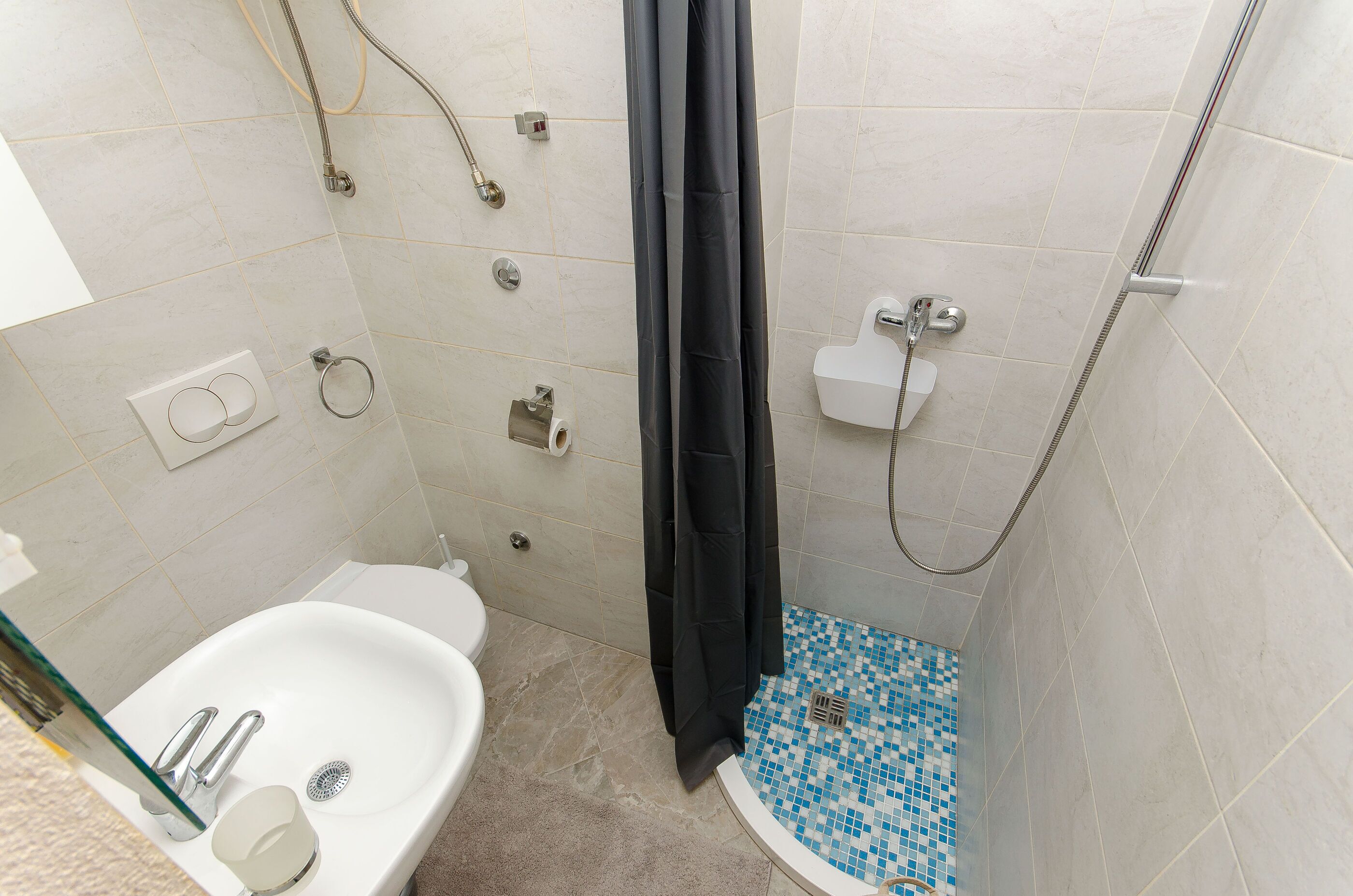 Un baño con lavamanos blanco, ducha con cortina negra y un inodoro.