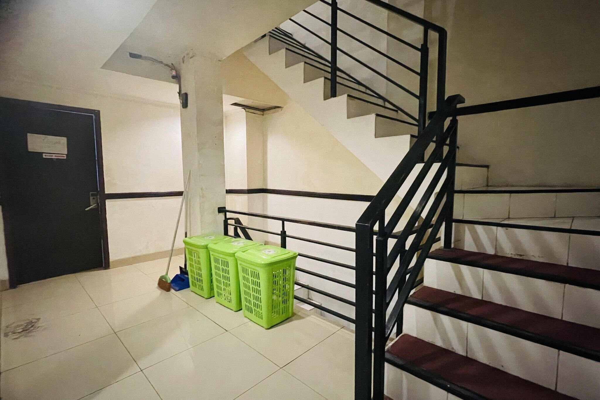 Un escalier avec des rampes noires, un balai et des paniers verts sur un sol carrelé.