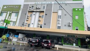 A hotel with multiple floors, air conditioning units, and a parking area with cars.