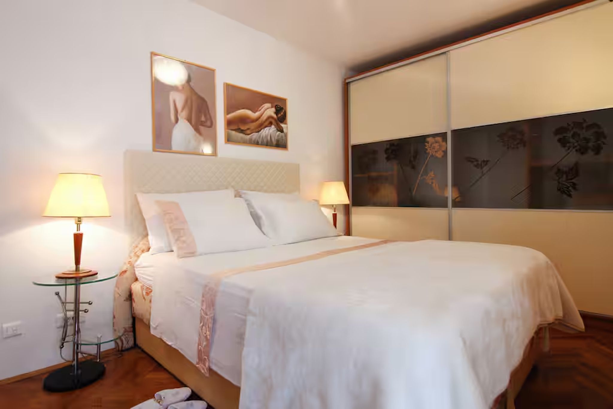 Ein Hotelzimmer mit einem großen Bett, zwei Nachttischlampen, einem Glastisch und Bildern an den Wänden.