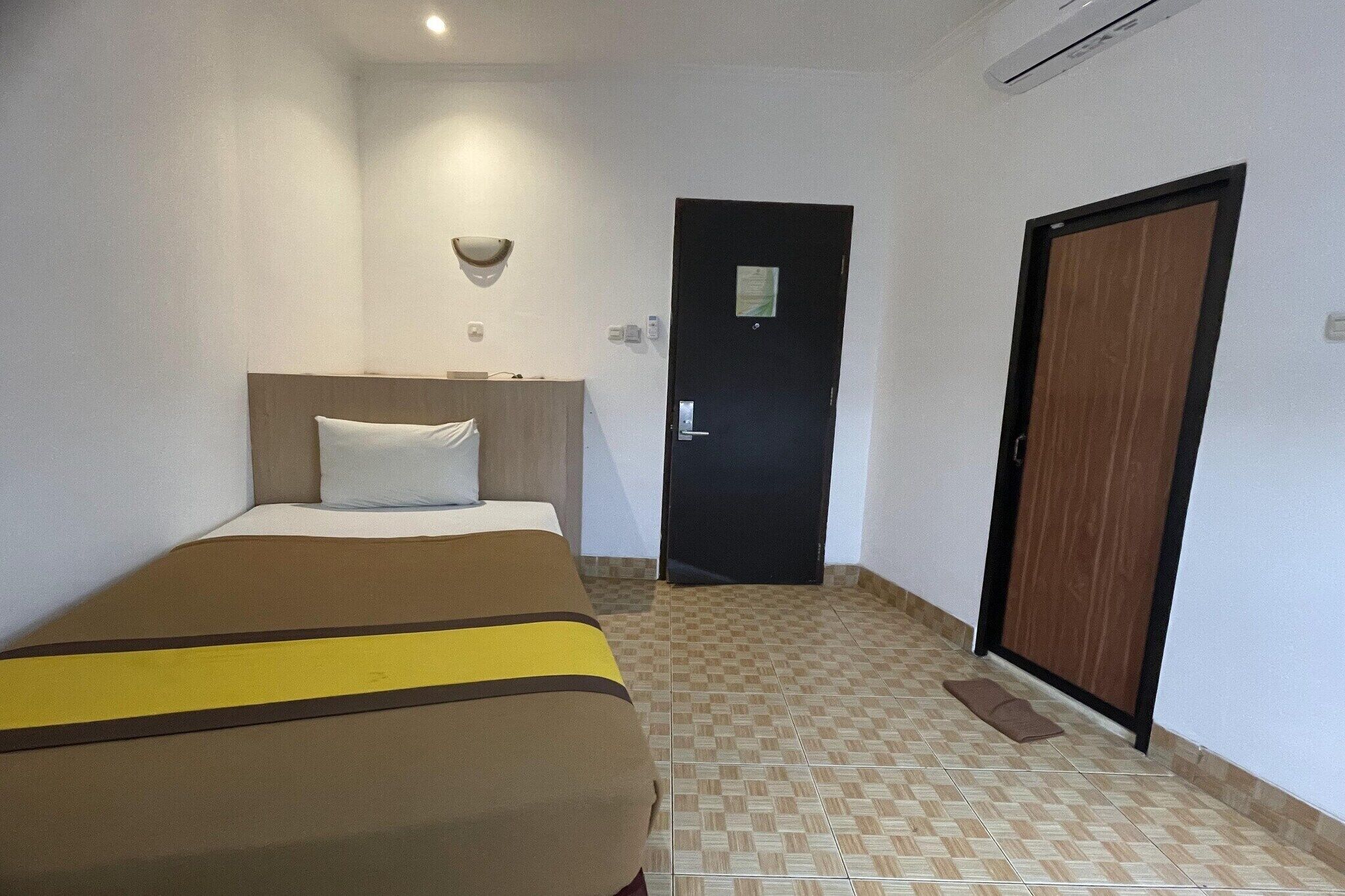 Une chambre d’hôtel avec un lit, une porte et un luminaire fixé au mur.