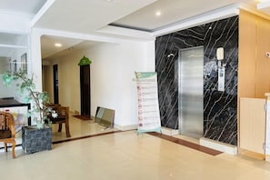 A hotel reception area with a marble wall, a reception desk, a plant, and an elevator.