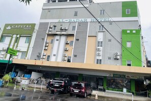 A hotel with multiple floors, air conditioning units, and a parking area with cars.