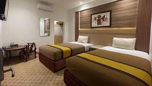 Ein Hotelzimmer mit zwei Betten, einem Schreibtisch, einem Stuhl, einem Fernseher und einem gerahmten Bild an der Wand.