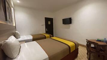 Ein Hotelzimmer mit zwei Betten, einem Fernseher, einer Tür und einem kleinen Tisch mit einem Stuhl.