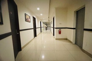 Ein Korridor mit Türen, einem Feuerlöscher und einer Treppe im Hintergrund.