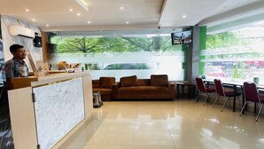 A hotel reception area with a marble counter, a brown sofa, and a dining area with red chairs. - Spacious DBL Suite Near Mall Panakkukang W/ WiFi (Makassar)