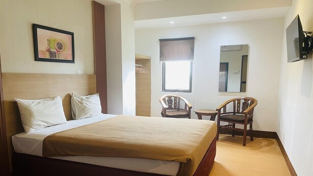 A hotel room with a bed, two chairs, a small table, a window with a view, and a wall-mounted TV. - Spacious DBL Suite Near Mall Panakkukang W/ WiFi (Makassar)