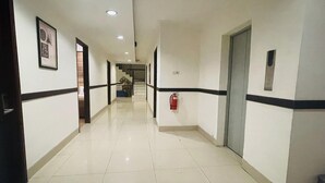 A long, narrow hallway with white walls and black trim, a fire extinguisher mounted on the wall, and a door at the end. - Spacious DBL Suite Near Mall Panakkukang W/ WiFi (Makassar)