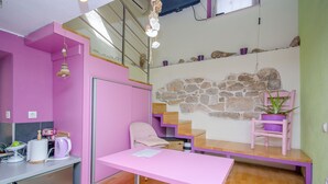 A pink desk with a chair, a small table, a potted plant, a stone wall, and a staircase. - Apartments Urban Stone Escape (Split)