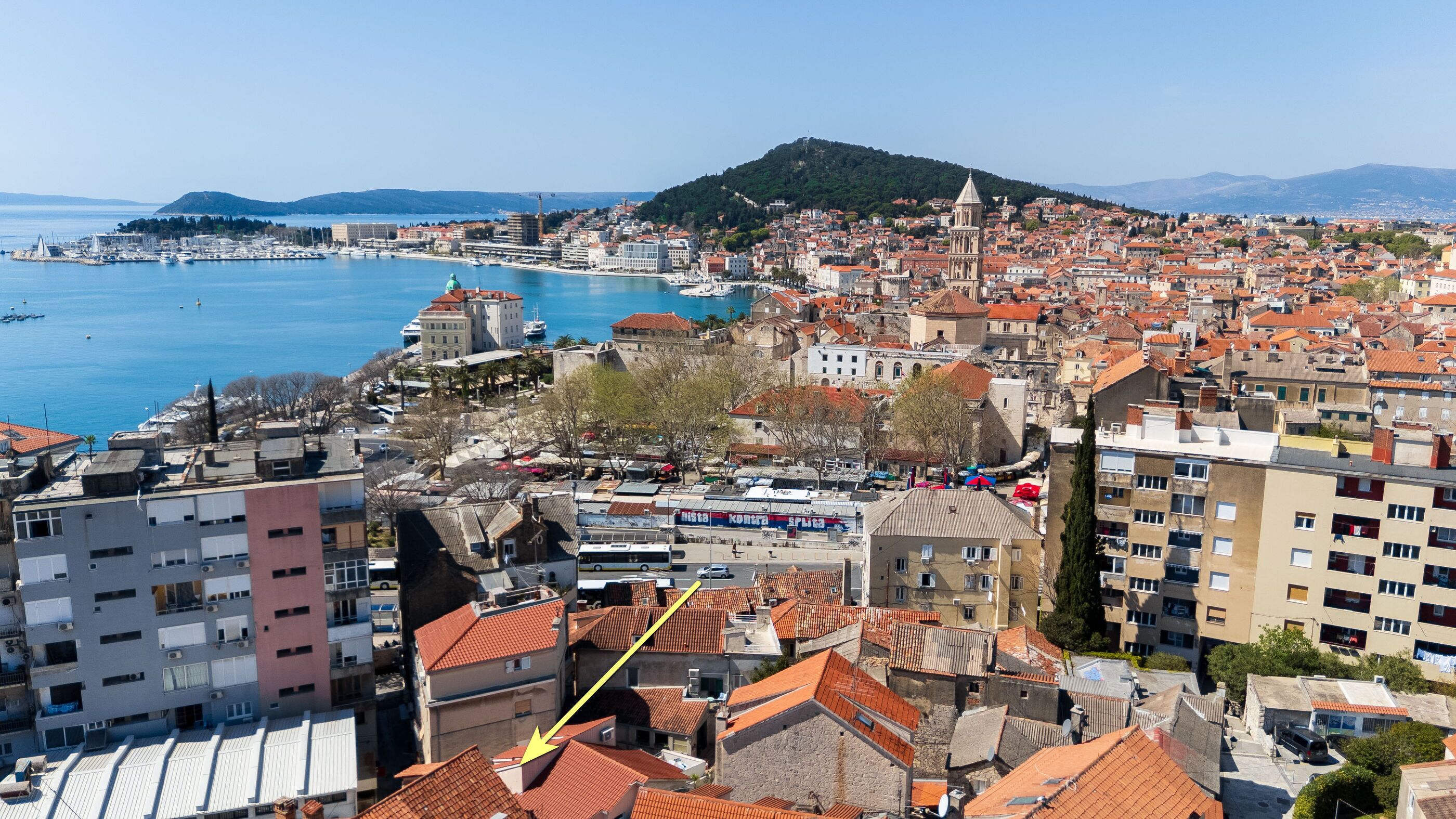 Un paisaje urbano costero con edificios históricos, un puerto deportivo y una colina al fondo.
