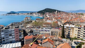 Paesaggio costiero con edifici storici, un porto turistico e una collina sullo sfondo.