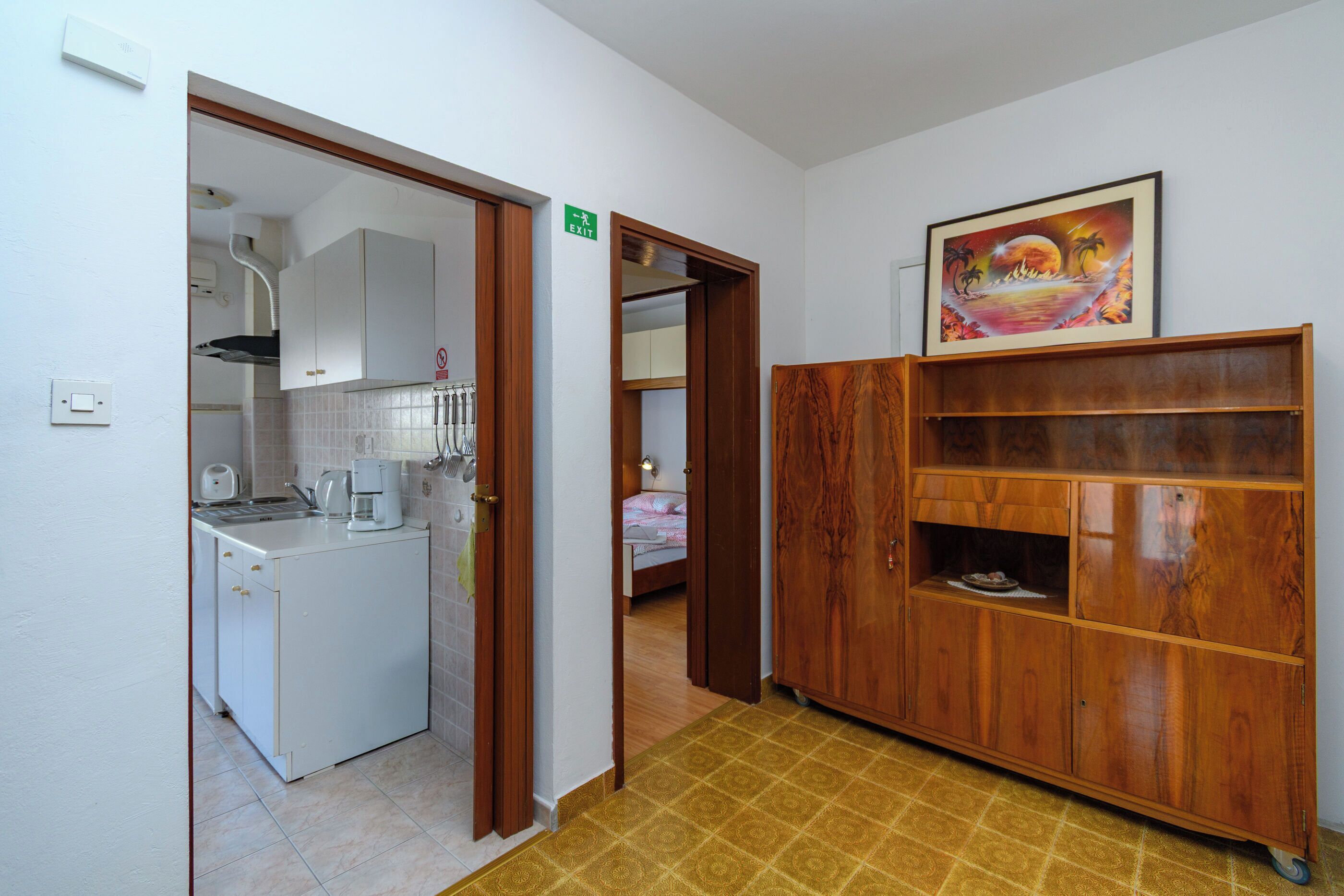 A kitchen with a coffee maker, a cabinet, and a door leading to a bedroom.