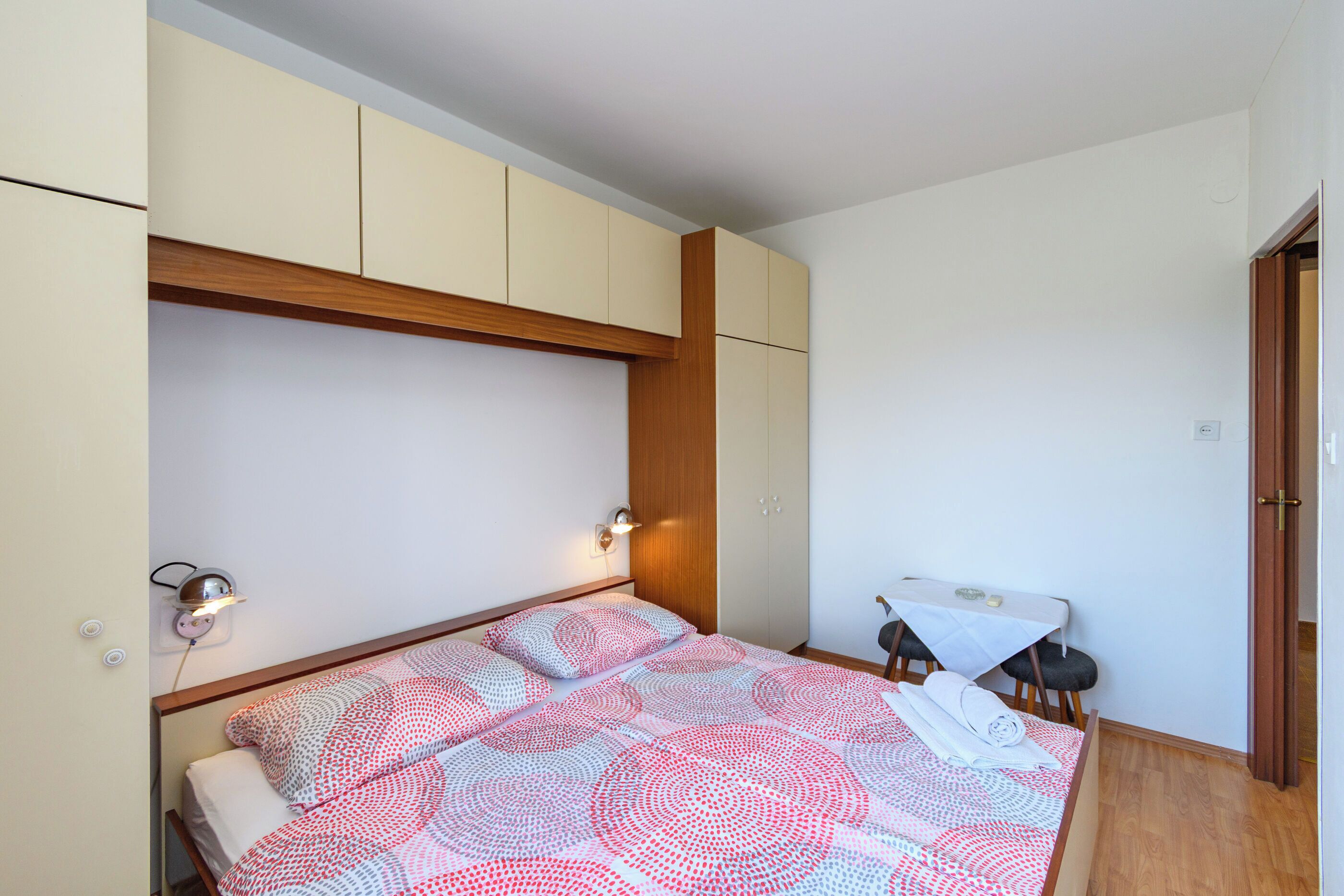 A bedroom with a bed, bedside tables, a small table, and a wardrobe.