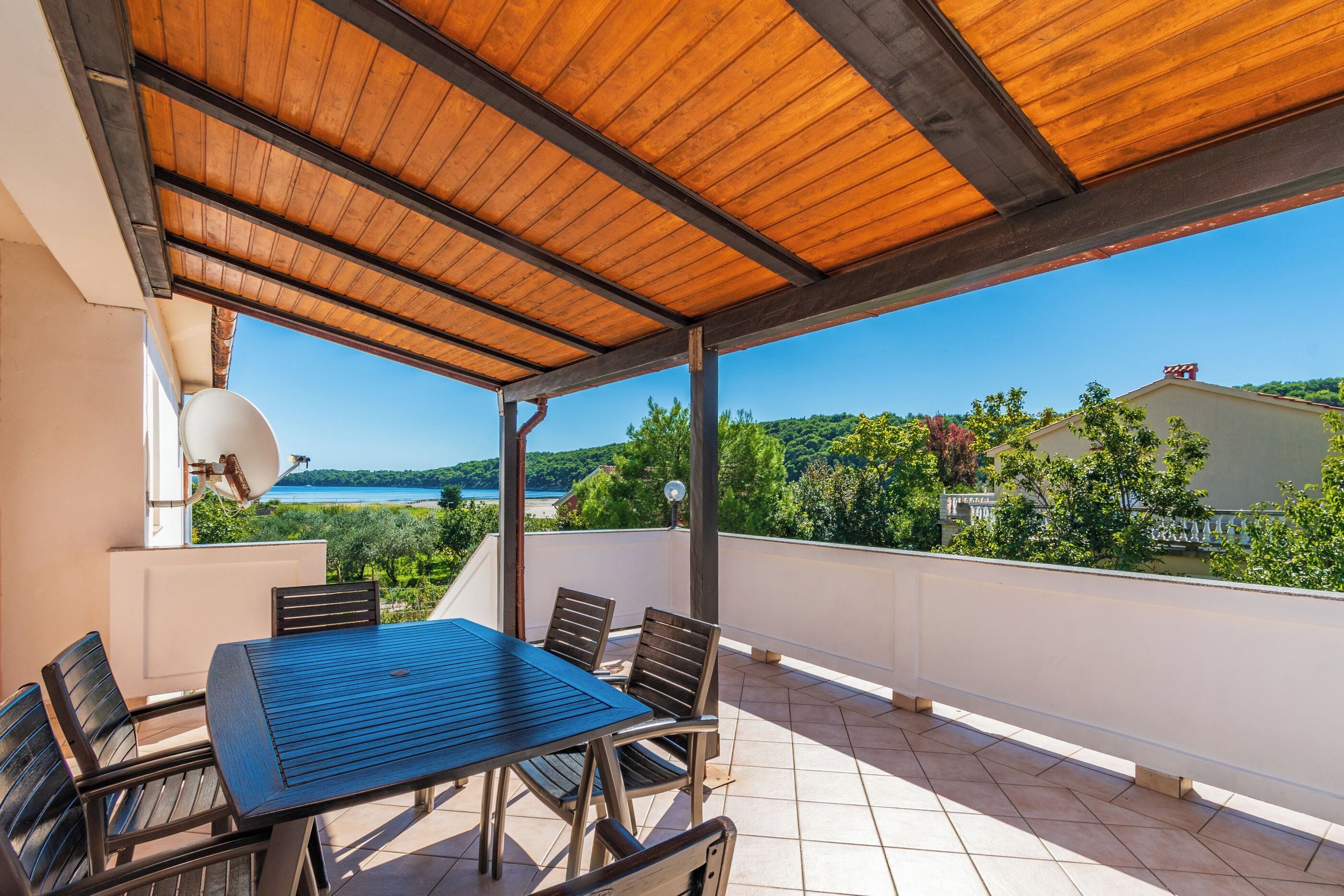 A covered outdoor seating area with a table and chairs, overlooking a scenic landscape.