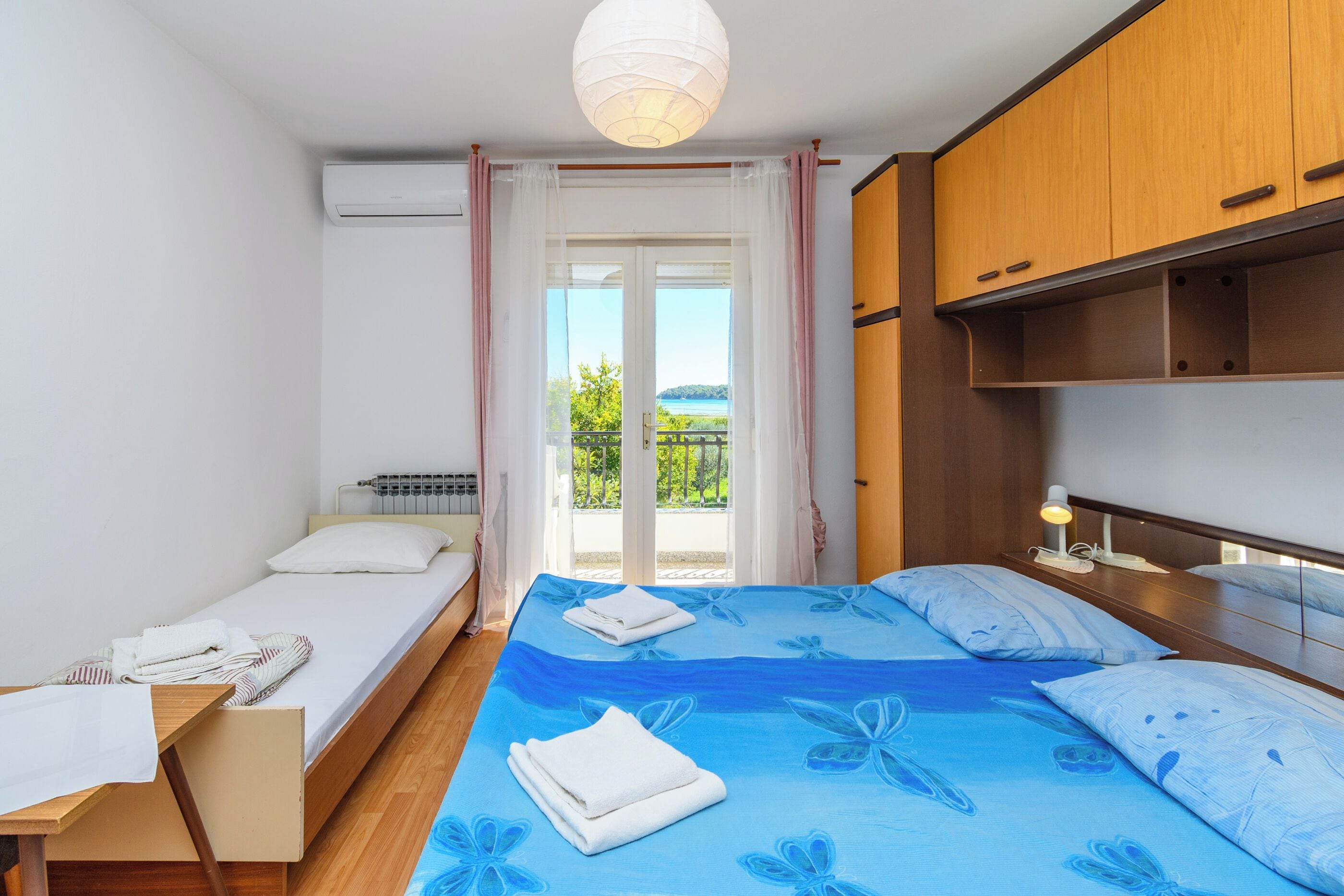 Une chambre à coucher comprenant un lit, une table de chevet, une lampe, une fenêtre avec des rideaux et une vue sur l’extérieur.
