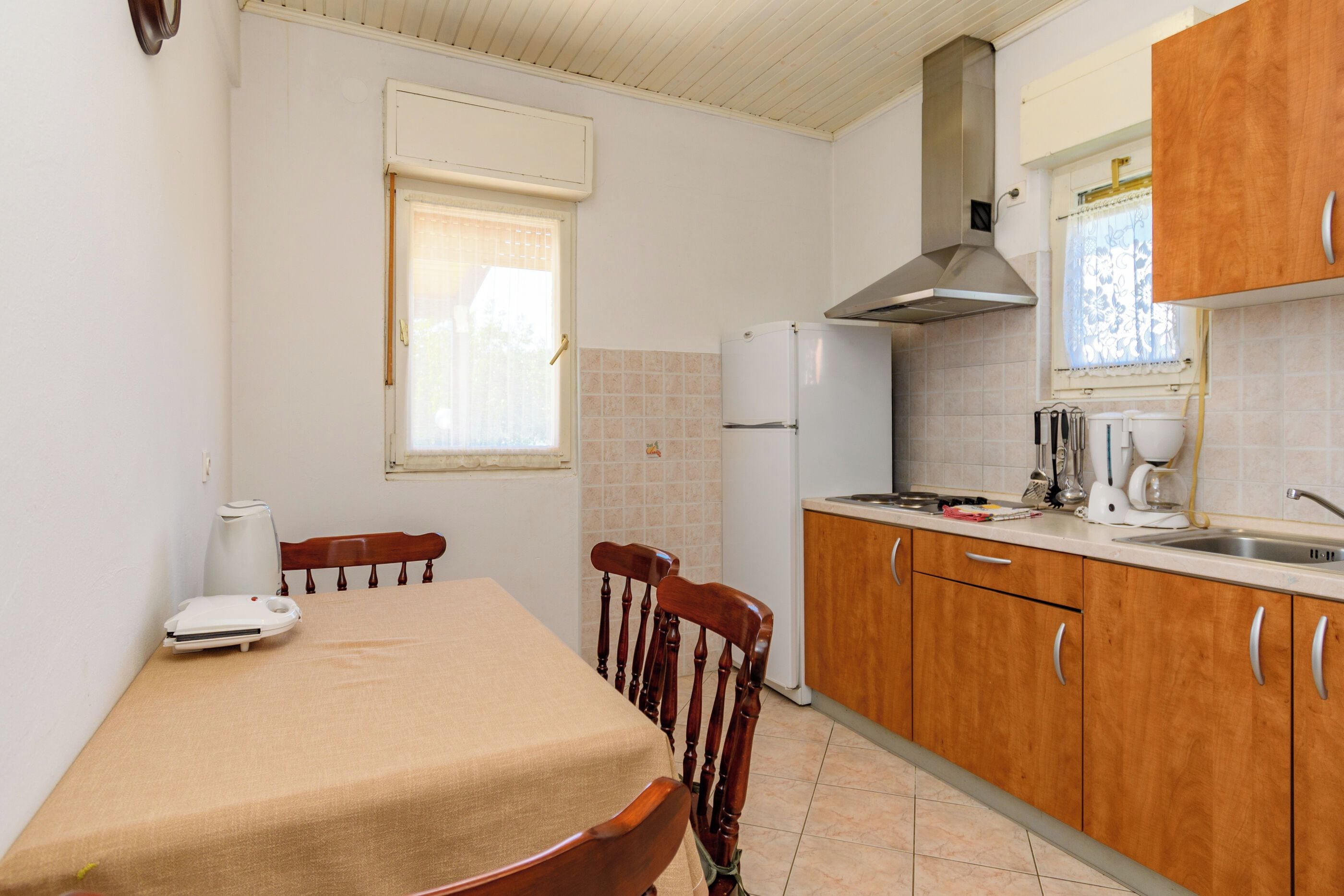 A compact kitchen with a dining table, chairs, a refrigerator, and a window.