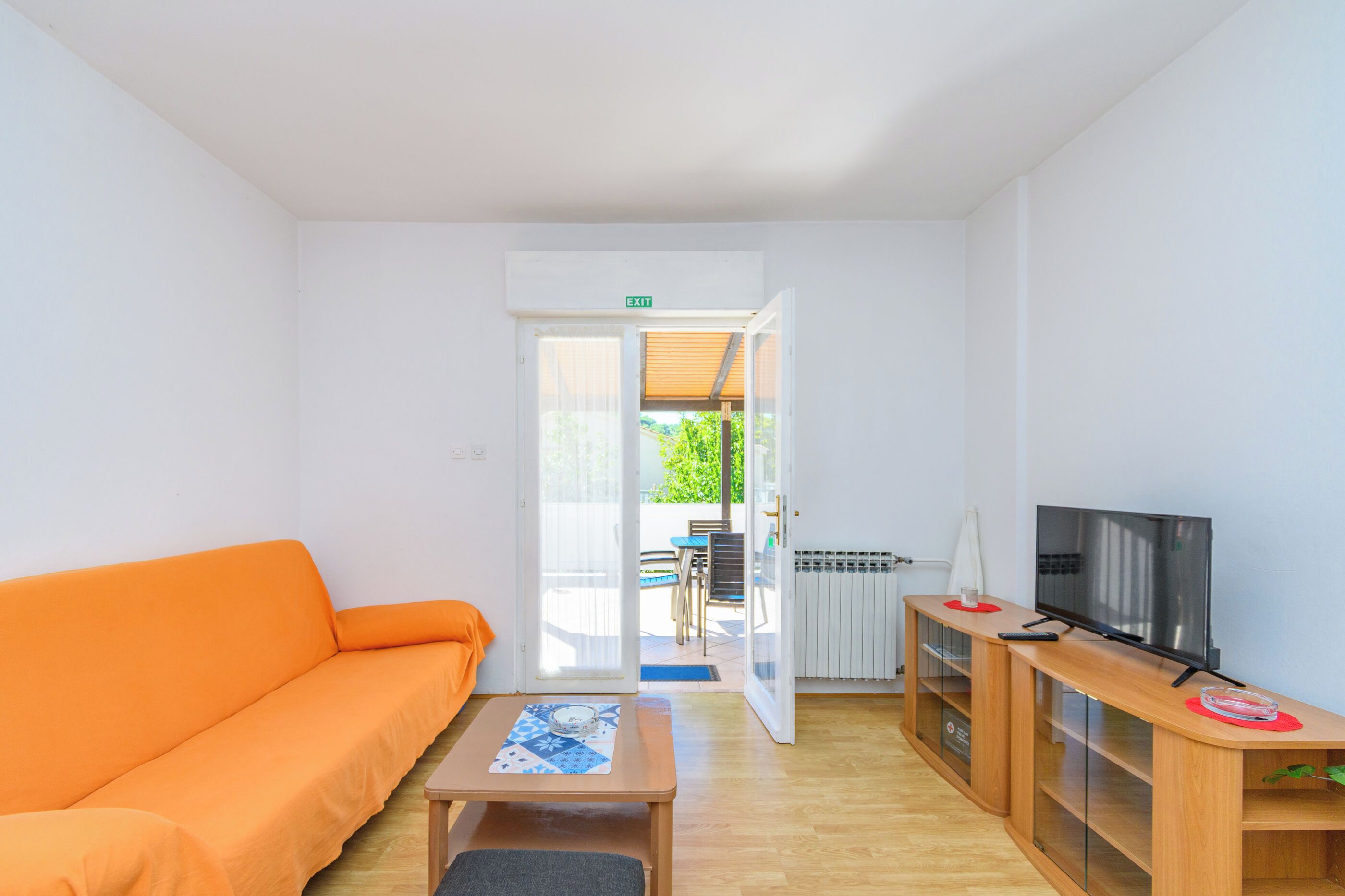 Quarto com sofá, televisão, uma pequena mesa e porta de saída para o exterior.