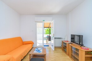 Una habitación con sofá, televisión, una mesita y una puerta de salida al exterior.