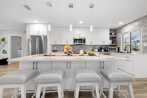 A modern kitchen with white cabinets, a central island with bar stools, and a stone backsplash. - Waterfront Pool Home w/ Gulf Access+Dock Sleeps 10 (Port Charlotte)