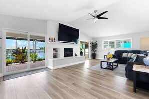 A modern living room with a flat-screen TV, a ceiling fan, and a view of the outdoors. - Waterfront Pool Home w/ Gulf Access+Dock Sleeps 10 (Port Charlotte)