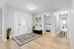 A hallway with a patterned rug, a potted plant, a cabinet, and a door with a decorative glass panel. - Waterfront Pool Home w/ Gulf Access+Dock Sleeps 10 (Port Charlotte)