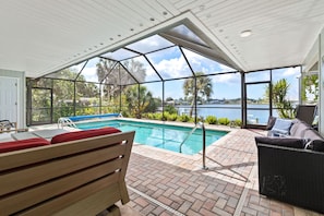 An indoor pool area with a view of a lake, a wooden bench, and a wicker sofa. - Waterfront Pool Home w/ Gulf Access+Dock Sleeps 10 (Port Charlotte)
