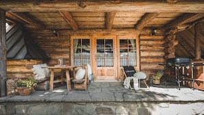 Una cabana de fusta rústica amb fonamentació de pedra, un porxo de fusta, una taula amb caires i una barbacoa.