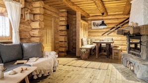 Interior d'una cabana de fusta amb sofà, taula i llar de foc.