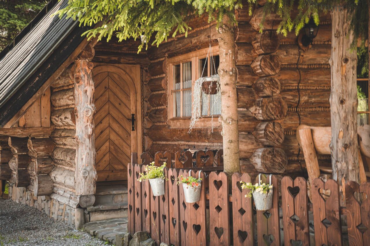 Une cabane rustique en rondins de bois, avec une porte en bois, une fenêtre et des jardinières en forme de cœur sur le porche.