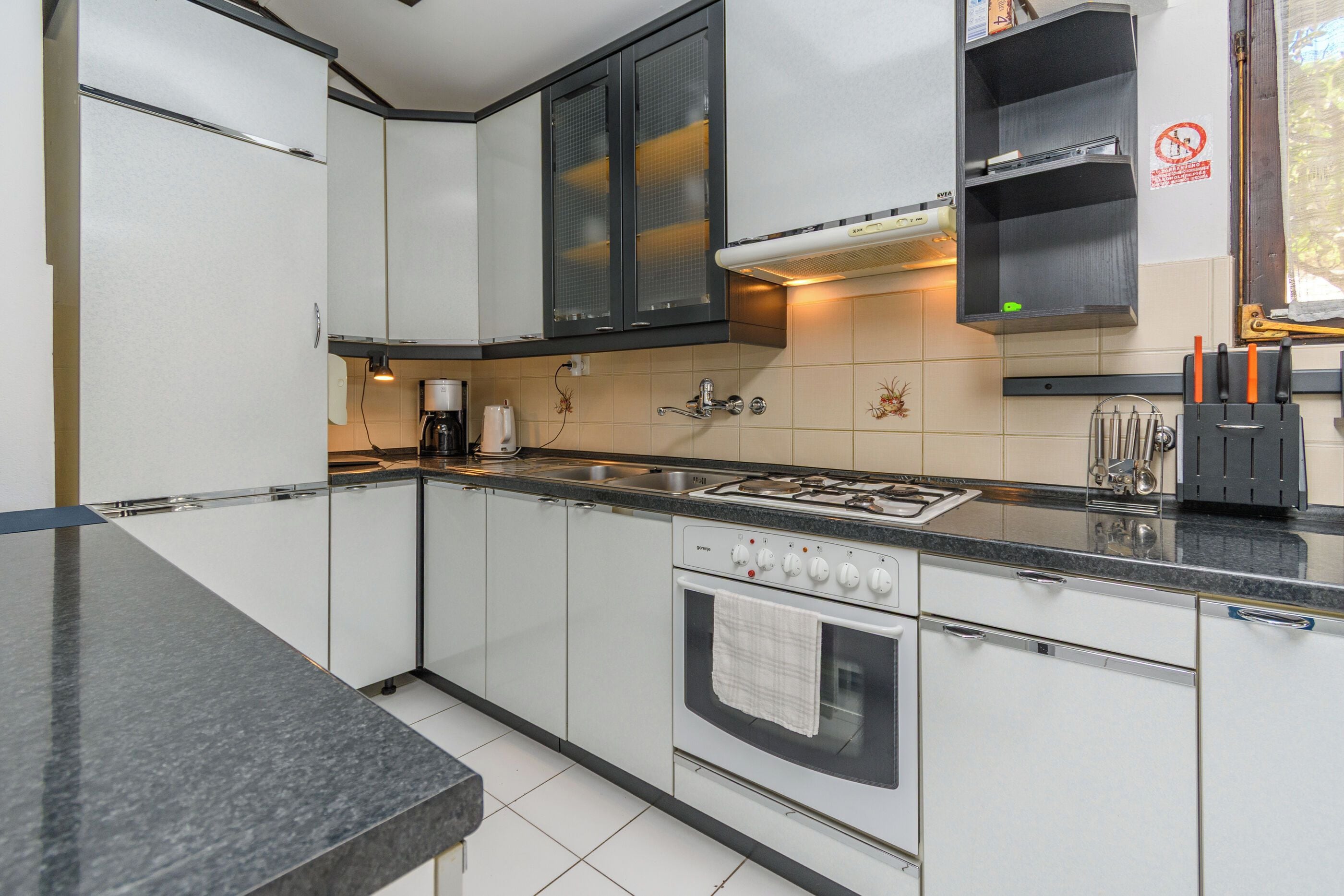A modern kitchen with white cabinets, a gas stove, and a coffee maker.