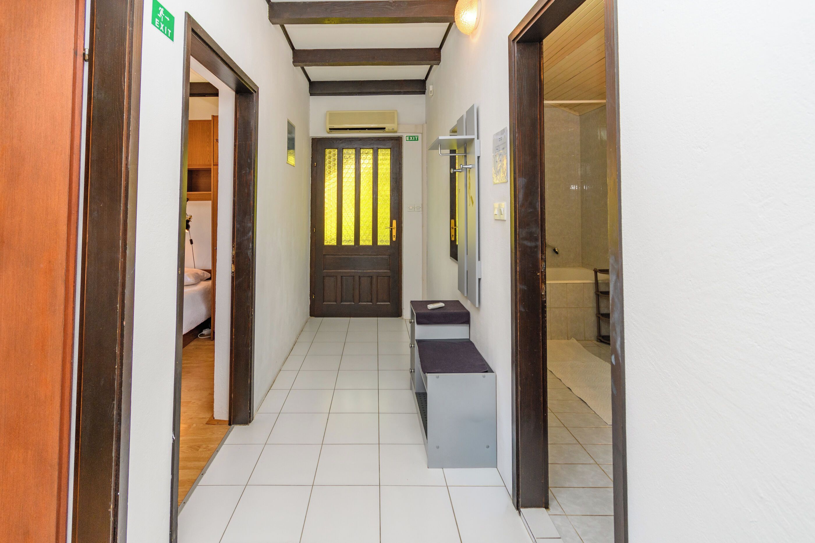 A hallway with a wooden door, a bench, and a tiled floor.