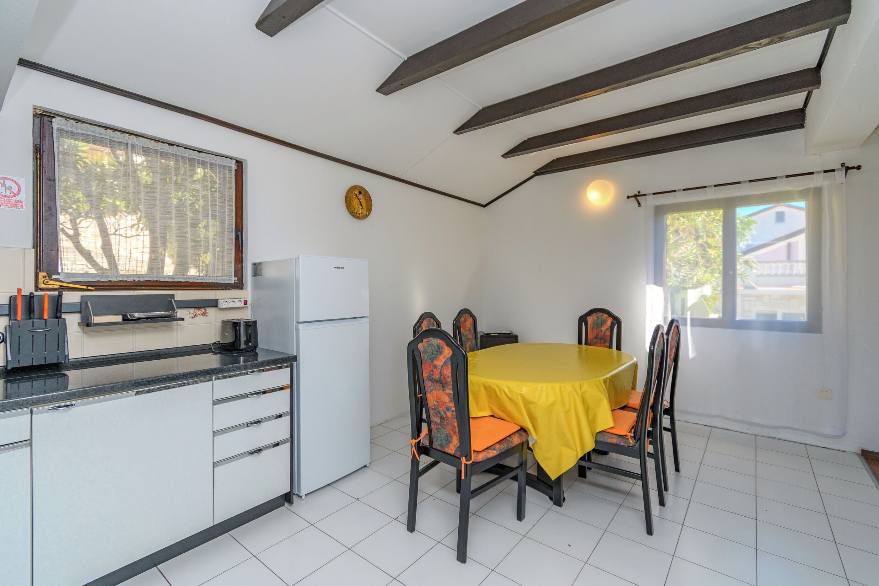 A compact kitchen with a dining area, featuring a table with chairs, a refrigerator, and a window with a view.