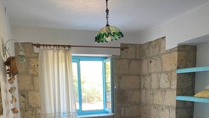 A room with two beds, a window with curtains, a stone wall, and a hanging light fixture. - Amazing Stone House in Ida Mountain-must See! (Ayvacik)