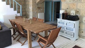 A dining area with a wooden table and chairs, a white cabinet with audio equipment, and a stone wall. - Amazing Stone House in Ida Mountain-must See! (Ayvacik)