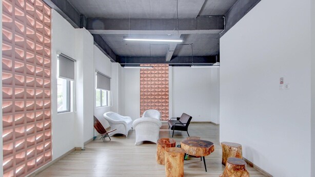 Un interior moderno con suelo de madera, paredes blancas y un revestimiento mural con diseño geométrico. Hay sillas blancas y una silla negra.