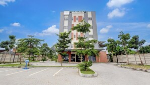 Un edificio moderno con el nombre 'INAWASENA' en la fachada, rodeado de una zona pavimentada con árboles y un cielo despejado.