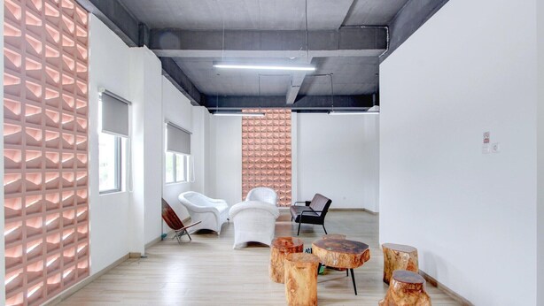 Een modern interieur met een houten vloer, witte wanden en een decoratief wandpaneel. Er staan verschillende stoelen en ronde houten tafels.